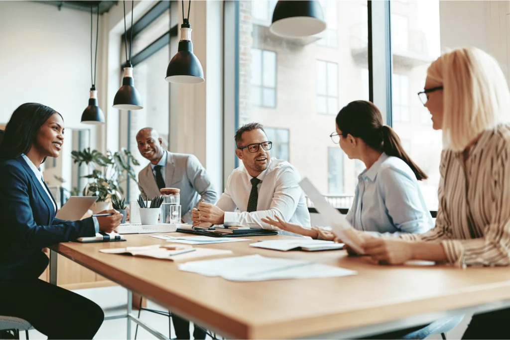 Réunion de direction avec une équipe diverse échangeant autour d’une table de travail pour démontrer diversité et performance